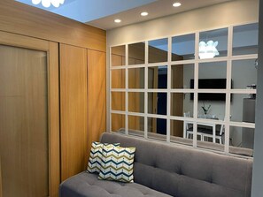 Ein modernes Wohnzimmer mit grauem Sofa, Holzwandverkleidung und einem großen Fenster mit vielen Glasscheiben.