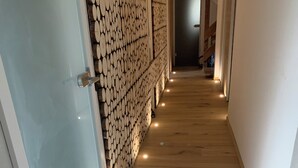 A hallway with wooden flooring, a wall of stacked logs, and recessed lighting.