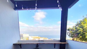 Ein Balkon mit zwei Stühlen, einem kleinen Tisch und Blick auf das Meer und Gebäude.