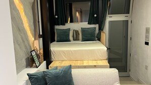 Ein Schlafzimmer mit einem Bett, einem Schlafsofa, einem Fenster mit Vorhängen, einer Tür und einer Wand mit LED-Beleuchtung.