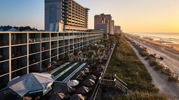 Un hôtel doté d’un espace piscine, offrant une vue sur la plage, et avec un immeuble de grande hauteur en arrière-plan.
