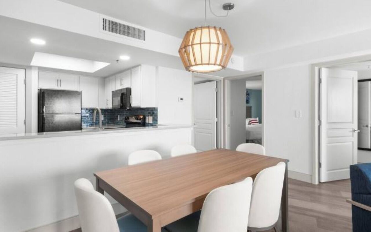 A modern kitchen with white cabinets, a black refrigerator, and a wooden dining table with white chairs.