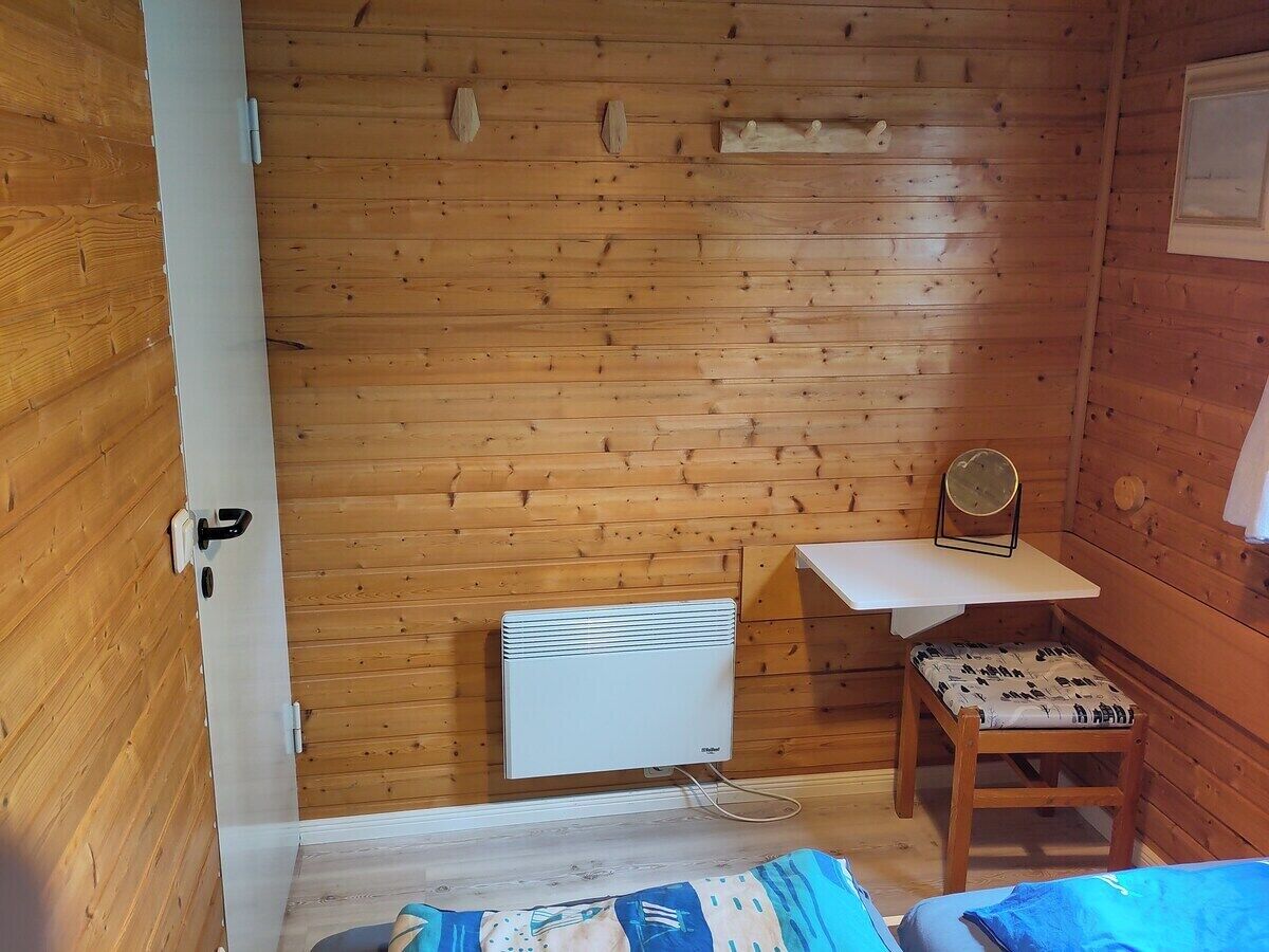 A small room with wooden walls, a white radiator, a table with a mirror, and a chair with a patterned cushion.