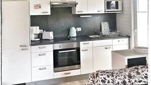 Een compacte keuken met witte kastjes, een magnetron, waterkoker en een kleine oven.