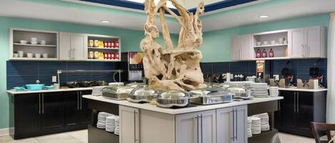 A modern kitchen with a central island, black cabinets, and a decorative tree sculpture.