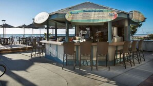 Un bar en bord de mer avec un tableau affichant le menu, des tables à l’extérieur et des parasols.