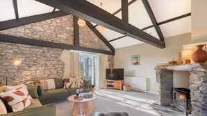 A cozy living room with a stone wall, a fireplace, a sofa, and a television. - The Royal Oak Barn Cartmel - Sleeps 4 (Cartmel)