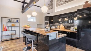 A modern kitchen with a central island, black cabinetry, and pendant lighting. - The Royal Oak Barn Cartmel - Sleeps 4 (Cartmel)