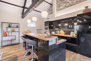 Une cuisine moderne dotée d’un îlot central, de meubles de couleur noire et d’un éclairage suspendu.