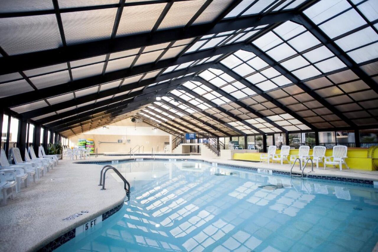 Une piscine intérieure dotée d’un toit en verre, de chaises longues blanches et offrant une vue dégagée sur l’ensemble de la piscine.