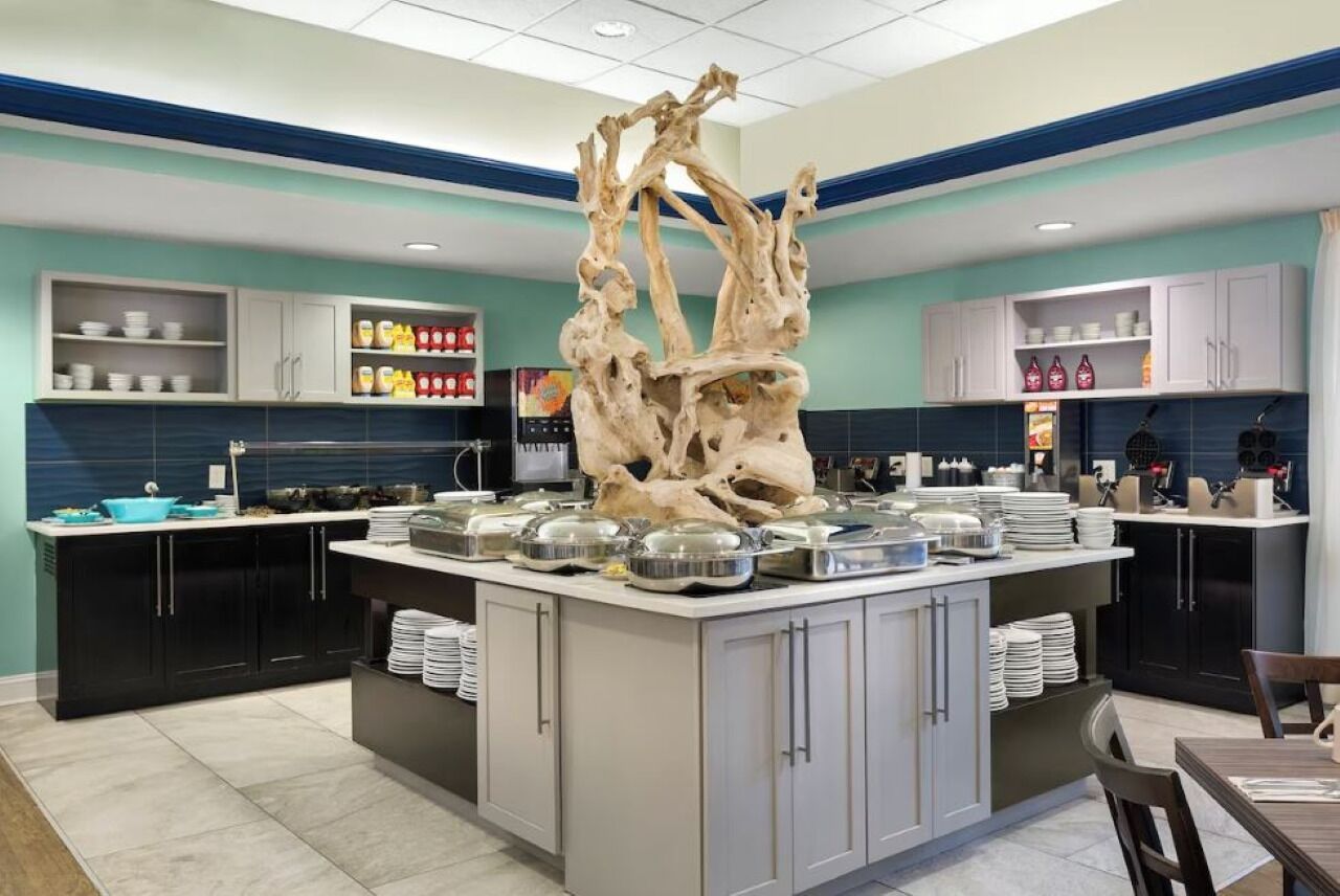 A modern kitchen with a central island, black cabinets, and a decorative tree sculpture.