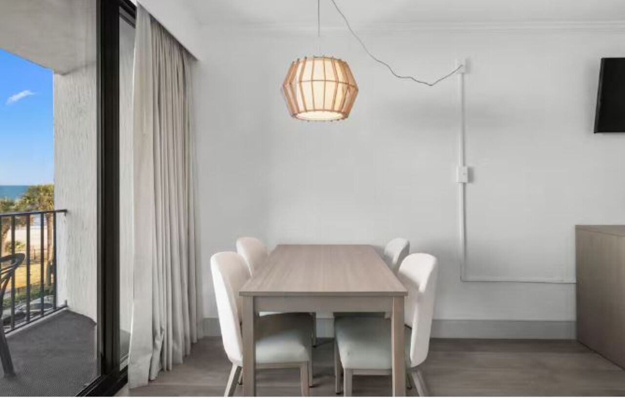Ett modernt matområde med ett träbord och vita stolar, en hängande lampa och utsikt över omgivningen.