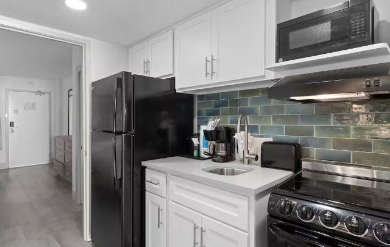 A modern kitchen with white cabinets, a black refrigerator, a stainless steel stove, and a microwave.