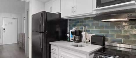 A modern kitchen with white cabinets, a black refrigerator, a stainless steel stove, and a microwave.