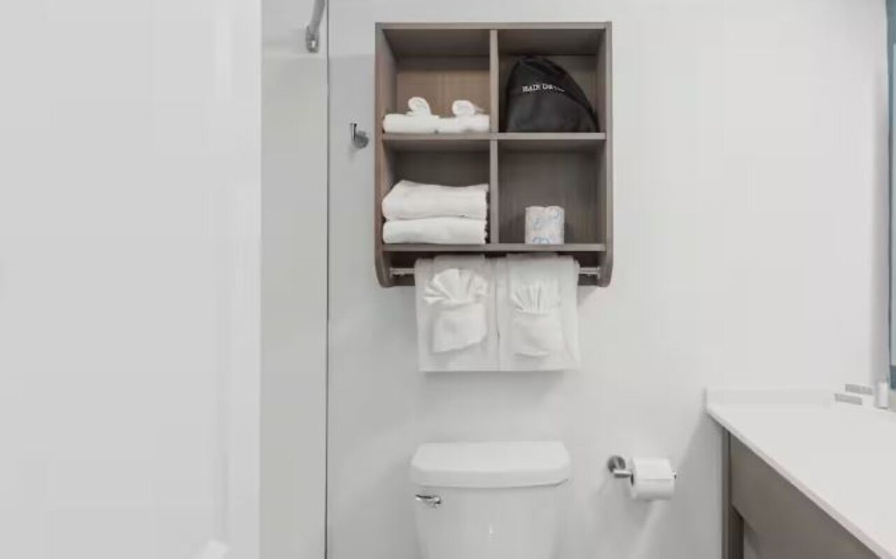 Un baño con inodoro, perchero y estante con toallas y una bolsa.