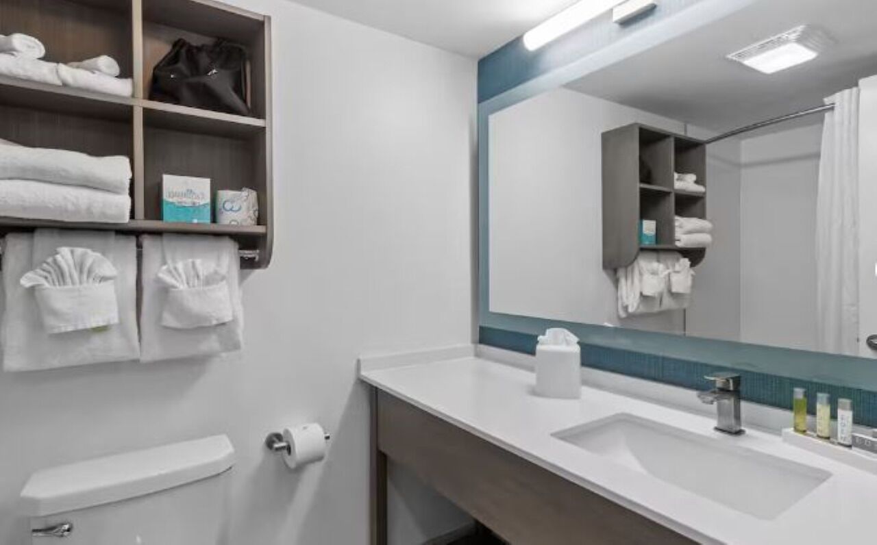 Uma casa de banho moderna com uma pia branca, um espelho e um porta-toalhas com toalhas dobradas.