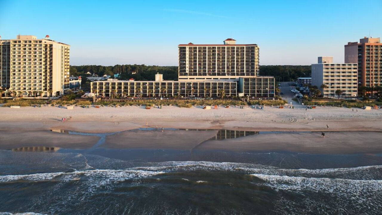 A beachfront hotel with multiple high-rise buildings, a sandy beach, and a calm sea.