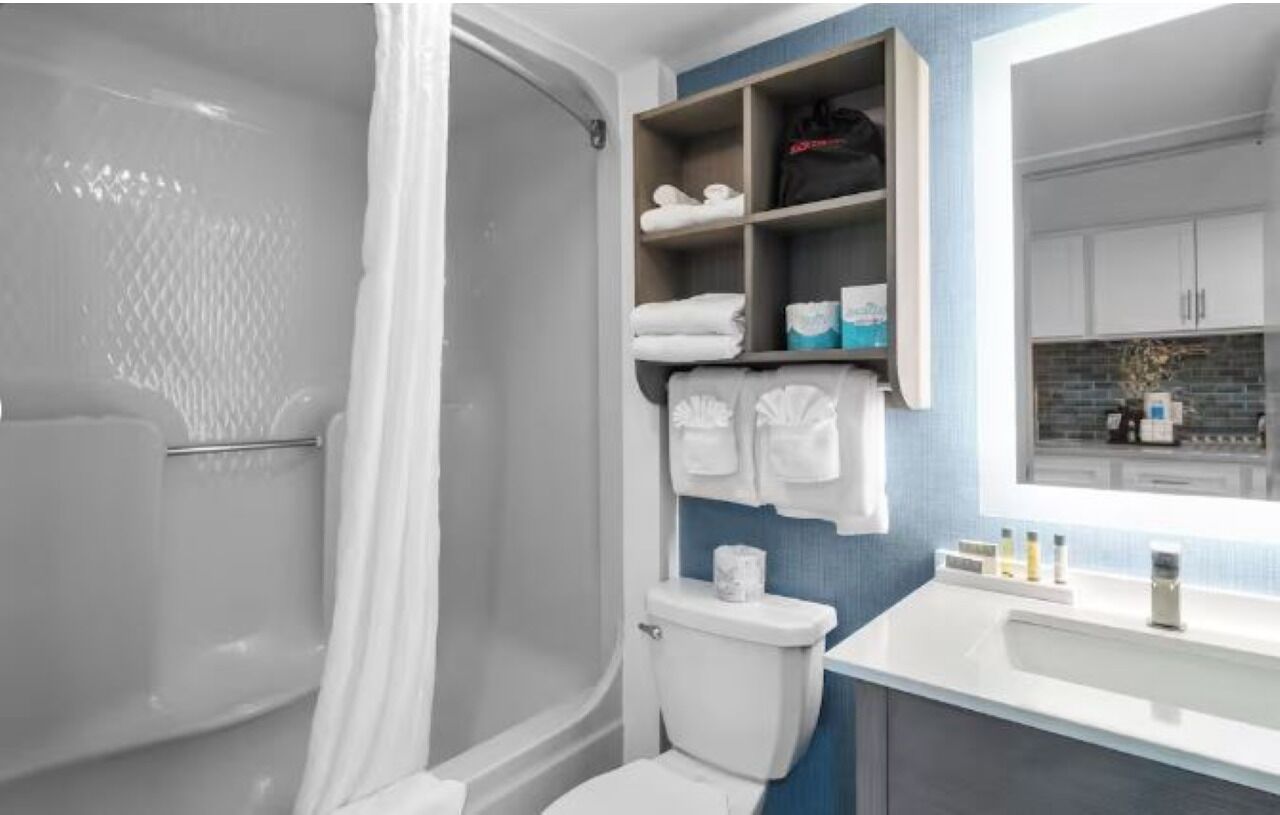 A bathroom with a shower, toilet, and sink. There are shelves with towels and toiletries.
