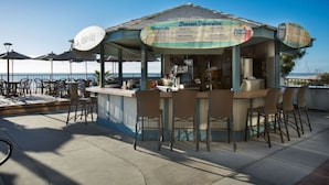 A seaside bar with a menu board, outdoor seating, and umbrellas. - Modern Oceanfront Retreat l 4 Units | Free Parking | Indoor and Outdoor Pools (Myrtle Beach)