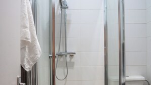 Eine begehbare Duschkabine aus Glas, eine weiße Toilette und ein Handtuch, das an der Tür hängt.