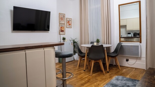 Eine moderne Küche mit Flachbildfernseher, einem Essbereich mit rundem Tisch und Stühlen sowie einem großen Spiegel.