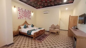 A bedroom with a patterned floor, a bed with a decorative headboard, a wall-mounted TV, and a ceiling with a detailed design. - Palette Hotel and Resort LBS INT (Pindra)