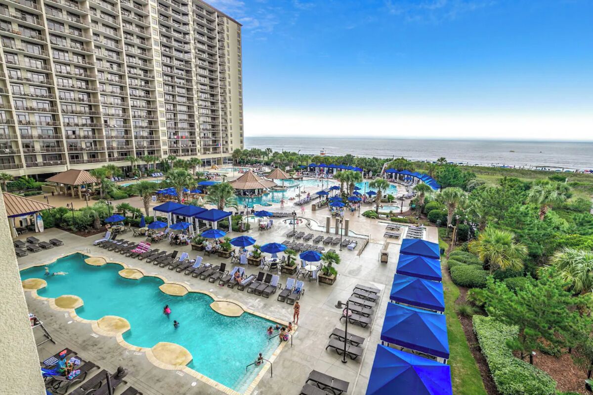 A hotel with a large pool area, multiple lounge chairs, and umbrellas.