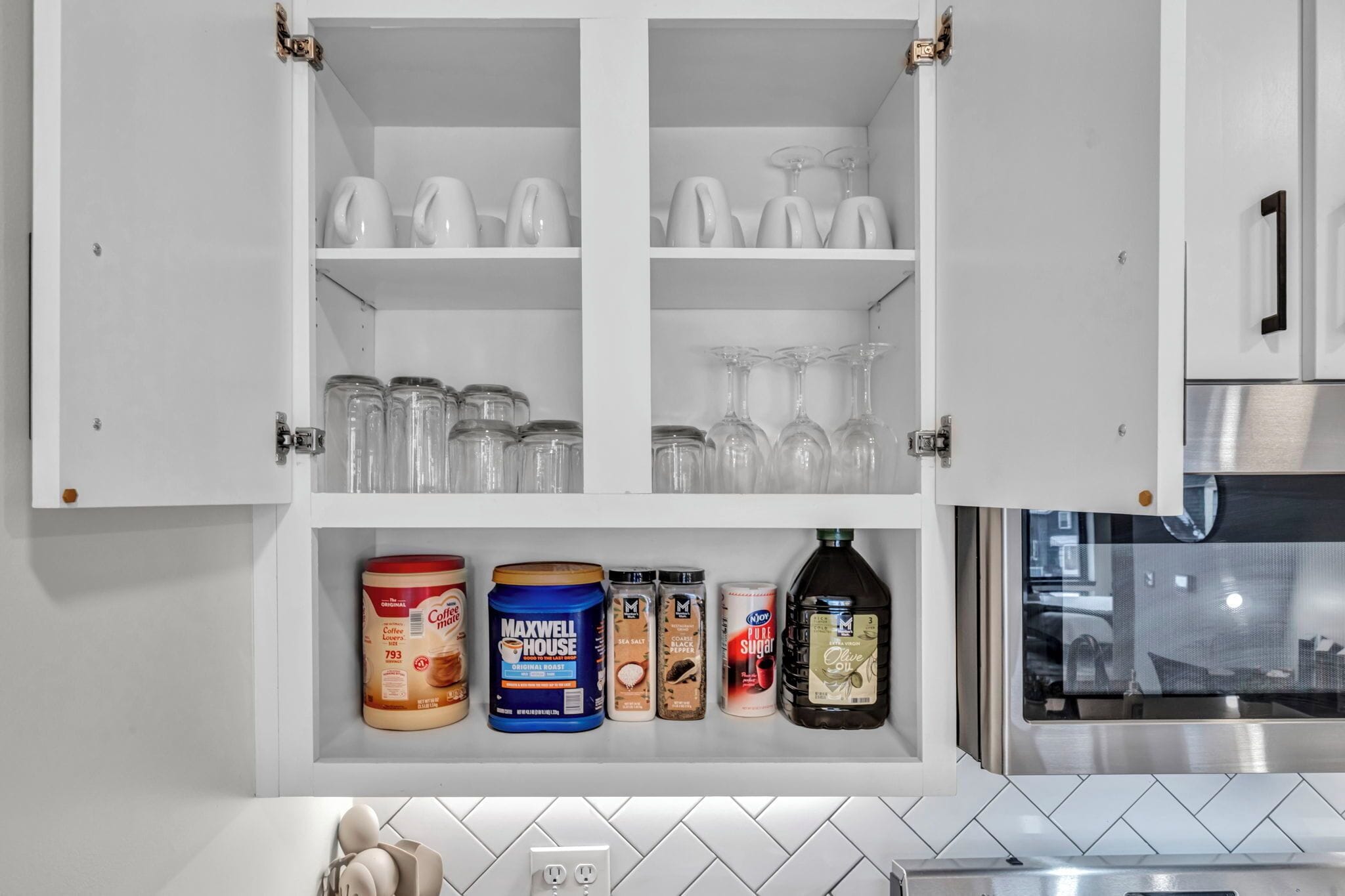 A kitchen with white cabinets, a coffee maker, a coffee pot, a tea kettle, a blender, and various food containers.
