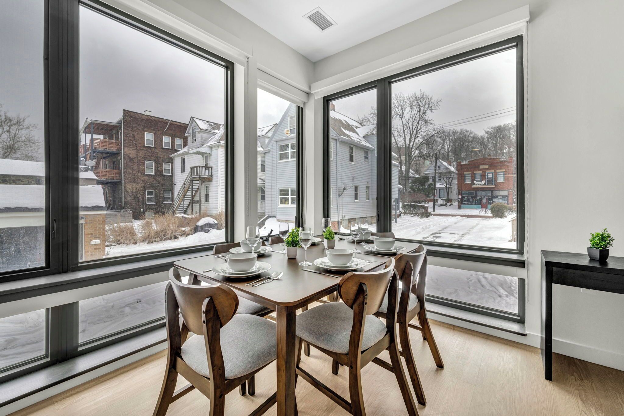A dining area with a large window overlooking a snowy neighborhood.