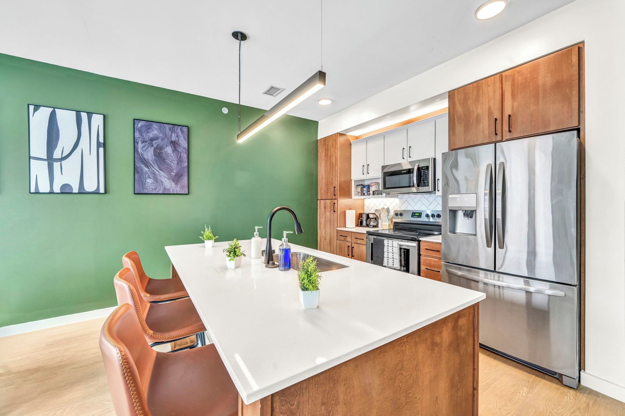 Une cuisine moderne dotée d’un îlot central, d’appareils électroménagers en acier inoxydable et d’un mur d’accent vert.