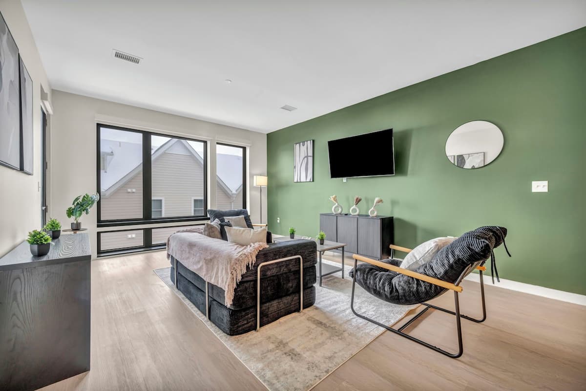 A modern living room with a sofa, a chair, a TV, and a green accent wall.
