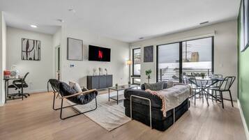 A modern living room with a sofa, armchair, dining table, and TV.