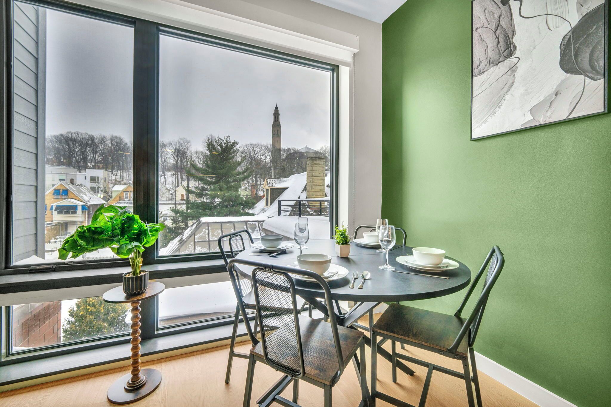 A dining area with a table set for two, a potted plant, and a view of a snowy landscape through large windows.
