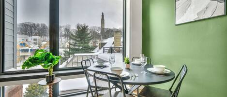 A dining area with a table set for two, a potted plant, and a view of a snowy landscape through large windows.