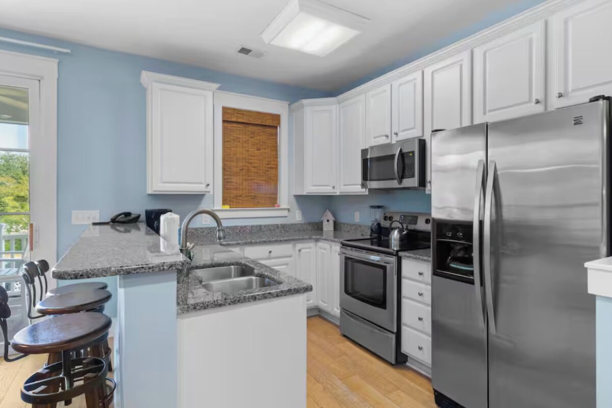 A modern kitchen with white cabinets, stainless steel appliances, a granite countertop, and a window with a view of greenery.
