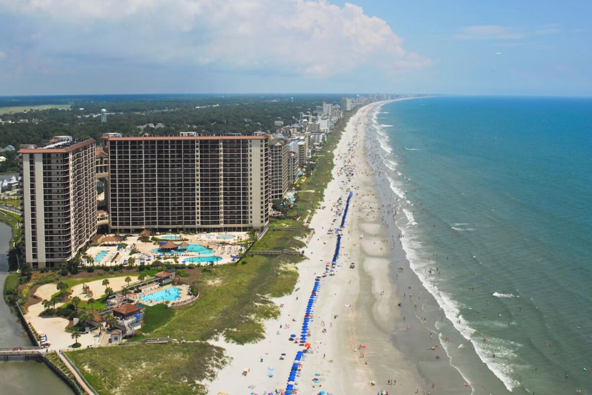 Un hotel costero con varios edificios altos, un largo paseo marítimo y una zona de piscina.