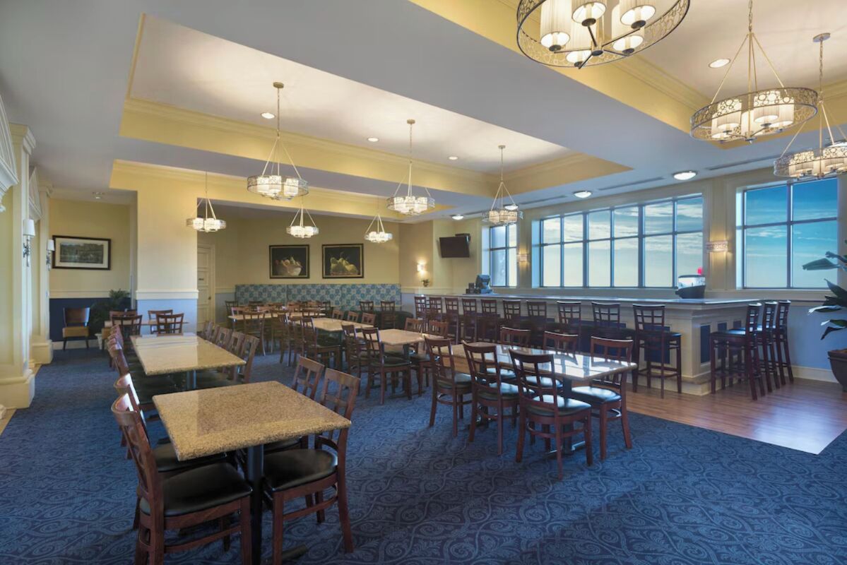 Un vaste espace dédié à la salle à manger, avec de nombreuses tables et chaises, des lustres et de grandes fenêtres qui laissent entrer la lumière naturelle.
