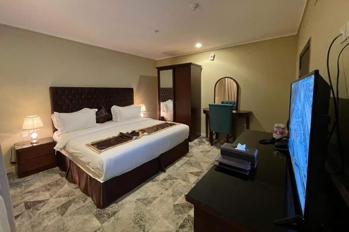 A hotel room with a large bed, a desk with a computer, a chair, and a mirror.