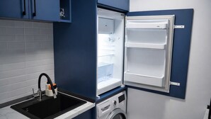 Une cuisine compacte équipée d’un lave-linge encastré, d’un évier avec un robinet et d’un réfrigérateur fixé au mur.