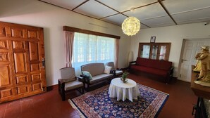 Una sala de estar con puerta de madera, sofás estampados, una mesa redonda con mantel blanco y una lámpara decorativa.
