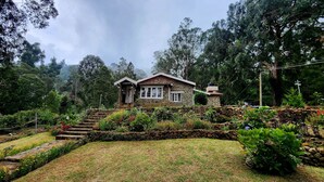 Una casa de piedra con techo inclinado, rodeada de abundante vegetación y una escalera de piedra que conduce a la entrada.