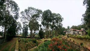 Una casa de piedra con tejado de tejas rojas rodeada de un jardín con diversas plantas y flores.