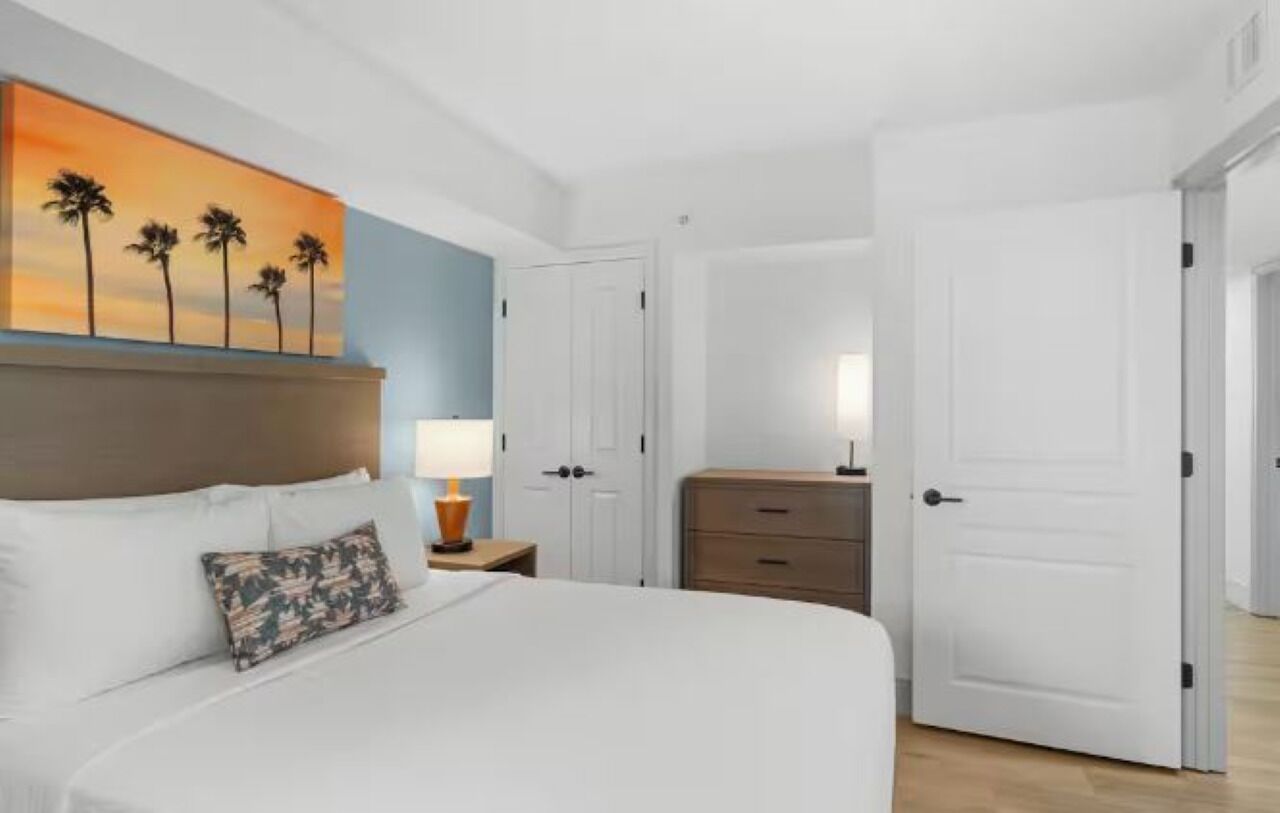Una habitación de hotel con cama, mesita de noche, lámpara, cómoda y puerta.