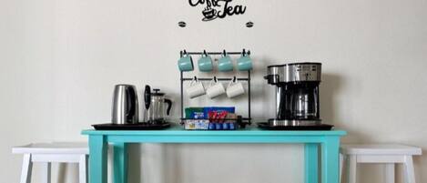 A teal coffee station with a coffee machine, mugs, and baskets.