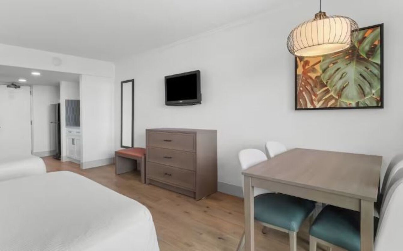 Une chambre d’hôtel comprenant un lit, un bureau avec des chaises, une télévision, une armoire et un tableau au mur.