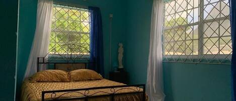 A room with a bed, a statue, and two windows with curtains.