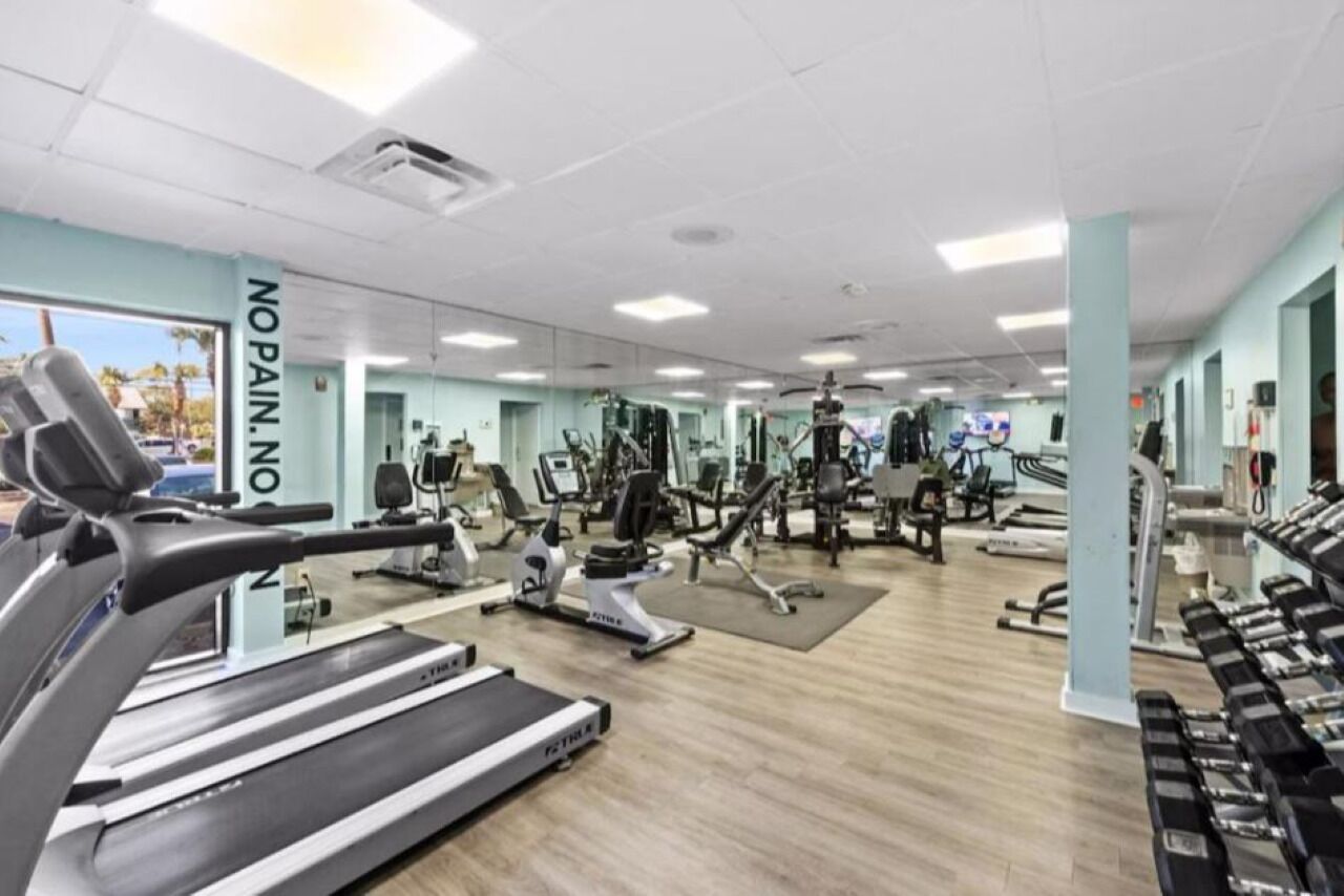 Une salle de sport équipée de tapis de course, d’appareils de musculation et d’un mur entièrement recouvert de miroirs.