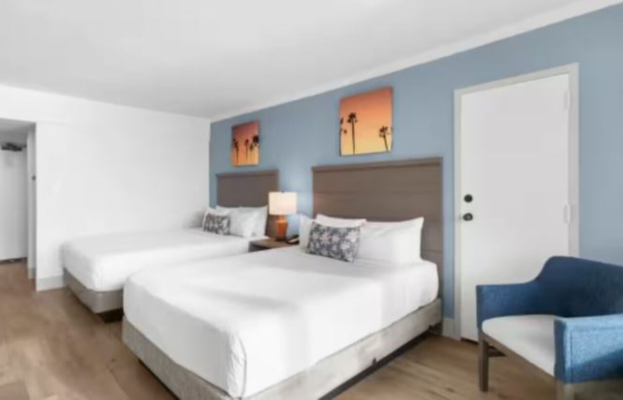 A hotel room with two single beds, a blue armchair, and artwork on the walls.