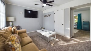 Una sala de estar con un sofá, un televisor, un ventilador de techo y una puerta que da a un balcón.