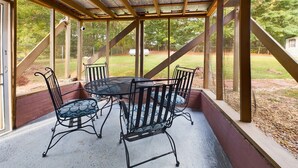 Un patio cubierto con mesa y sillas, vigas de madera y vista al jardín.